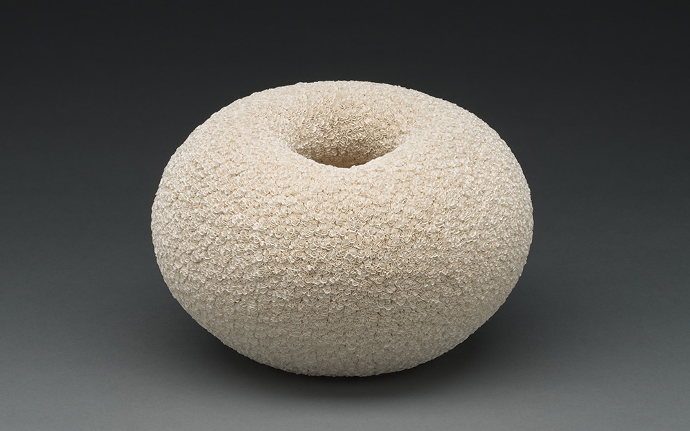 A donut-shaped sculpture with a scaly, beige surface