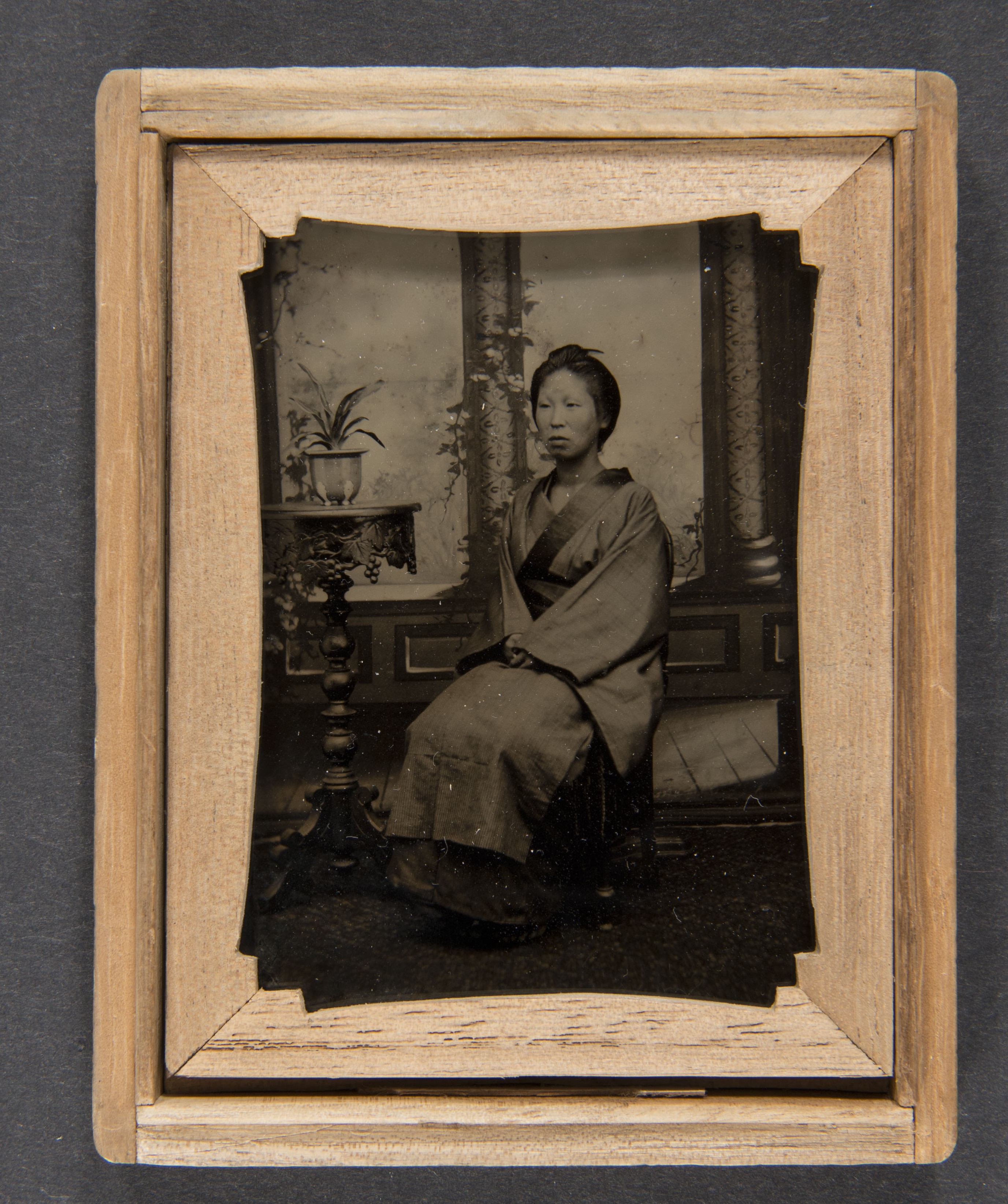 black and white photograph of a Japanese woman in a robe sitting next to an end table with a small plant