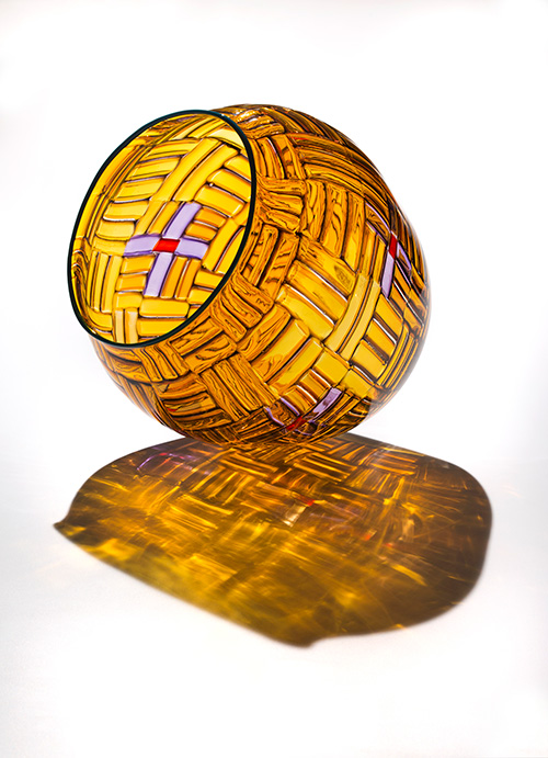 A clear yellow glass vessel that looks like a woven basket with white cross details with red centers
