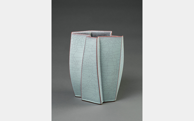 An angular ceramic vessel with a cracked, light blue glaze