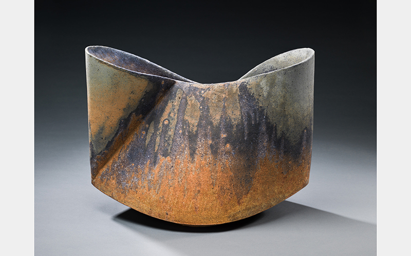 A ceramic form looking like a pinched bowl with a rough, rust-colored glaze