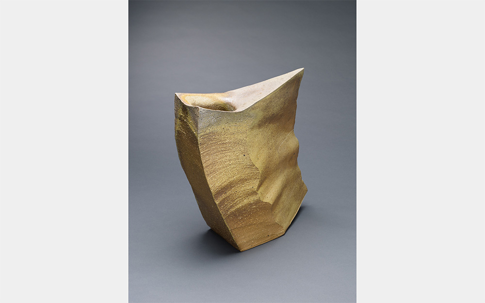 A gold sculpture with a squared side and a sharp, angled side