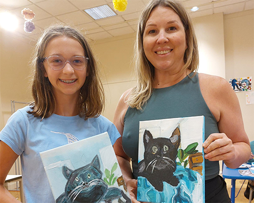A white mother and daughter hold their paintings of cats