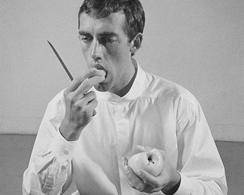 A white man eats an apple slice while holding a knife
