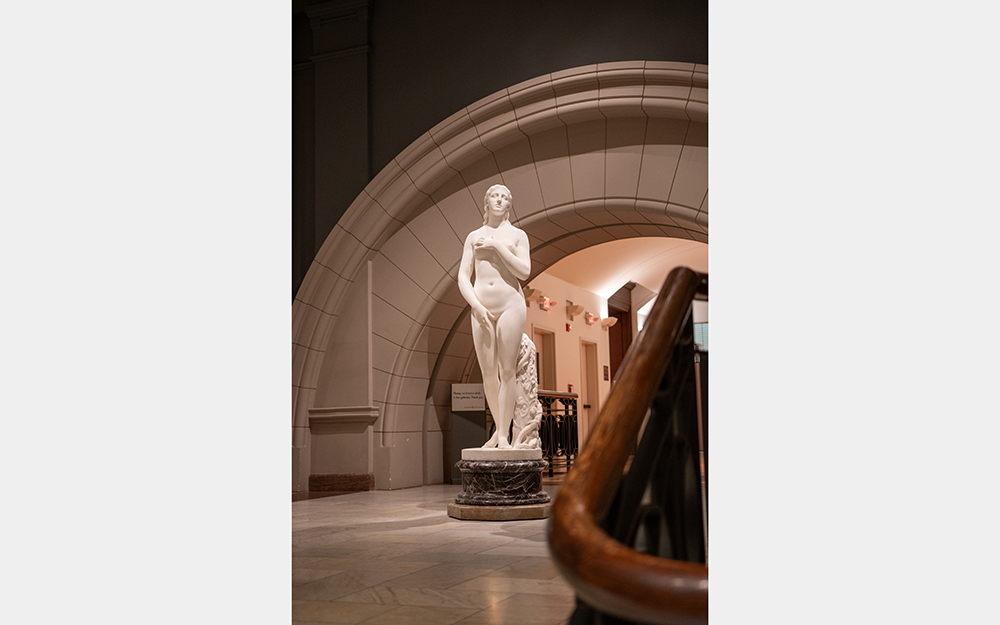 A photo of a white statue of a nude woman covering her body with her arms