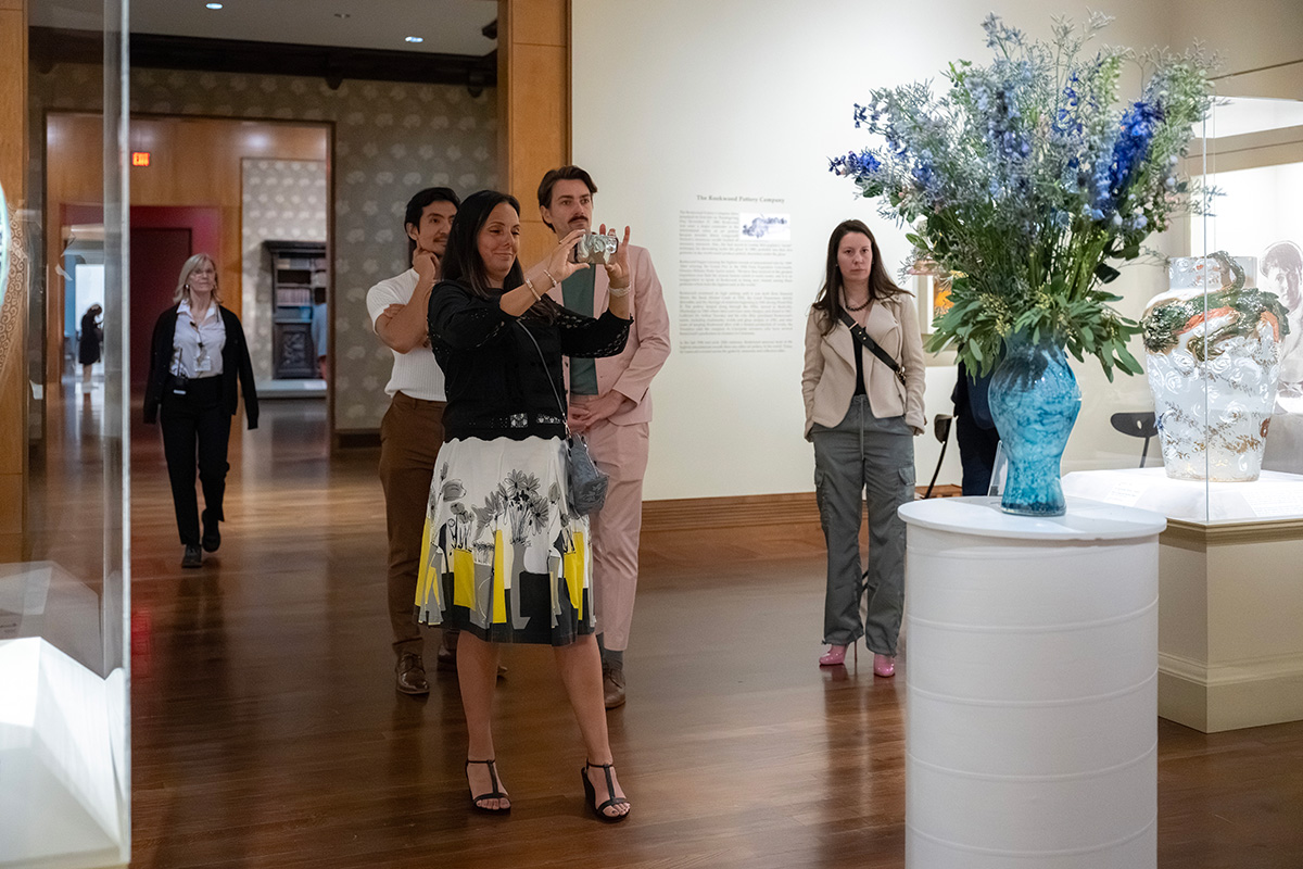 A visitor takes a photo of a flower arrangement while other visitors watch