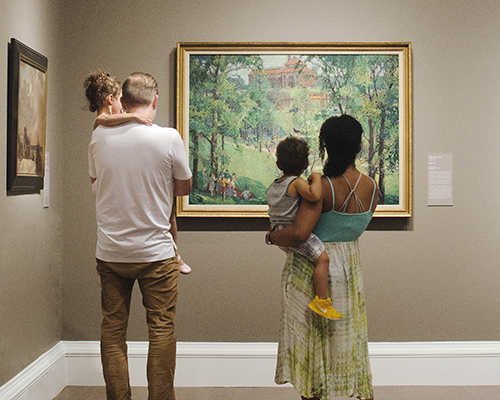 A couple holding kids looks at an artwork