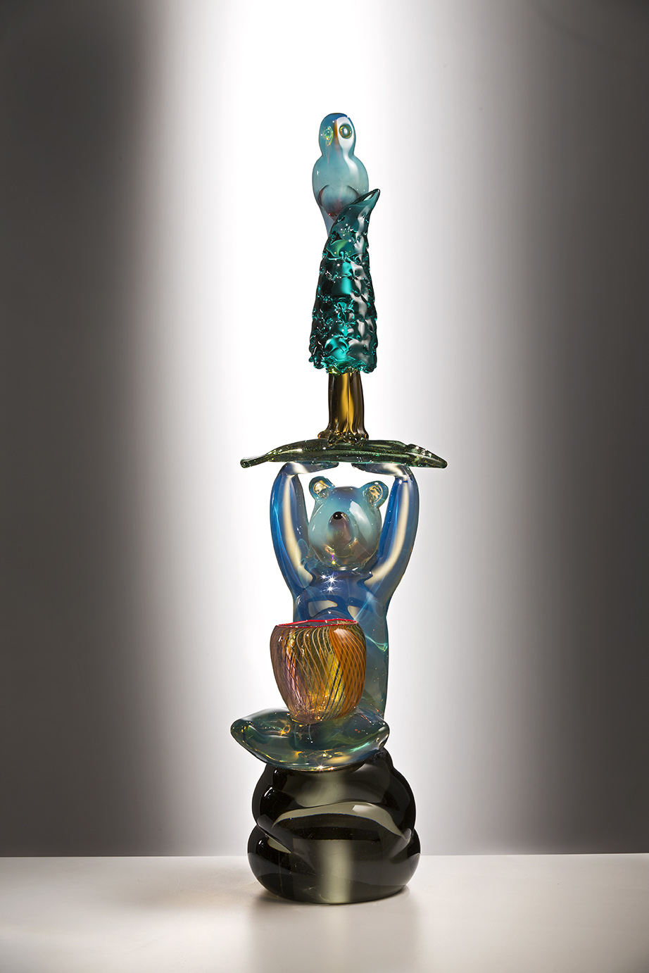 A glass sculpture featuring a bear holding up a tree with a bird at the top