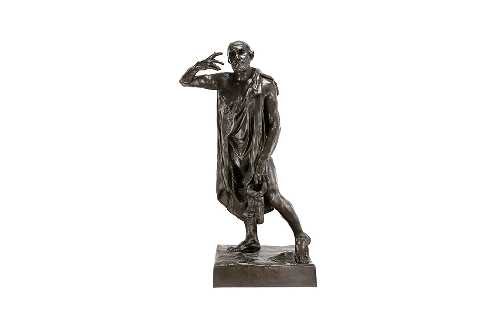 A dark, rough sculpture of a man in a robe. The man is mid-step, with their open hand reaching towards their face.