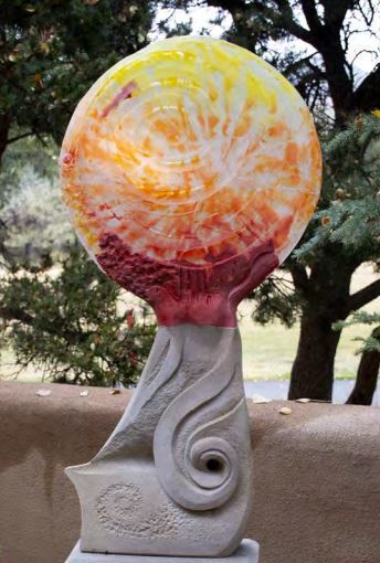 Chaco Sunrise is a large three-dimensional sculpture crafted from glass and stone. A round glass disk, representing the sun, grows out of a gray, wave-shaped stone.