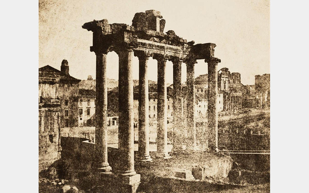 Ruins of a classical era building featuring 7 columns holding up an architrave with buildings in the background