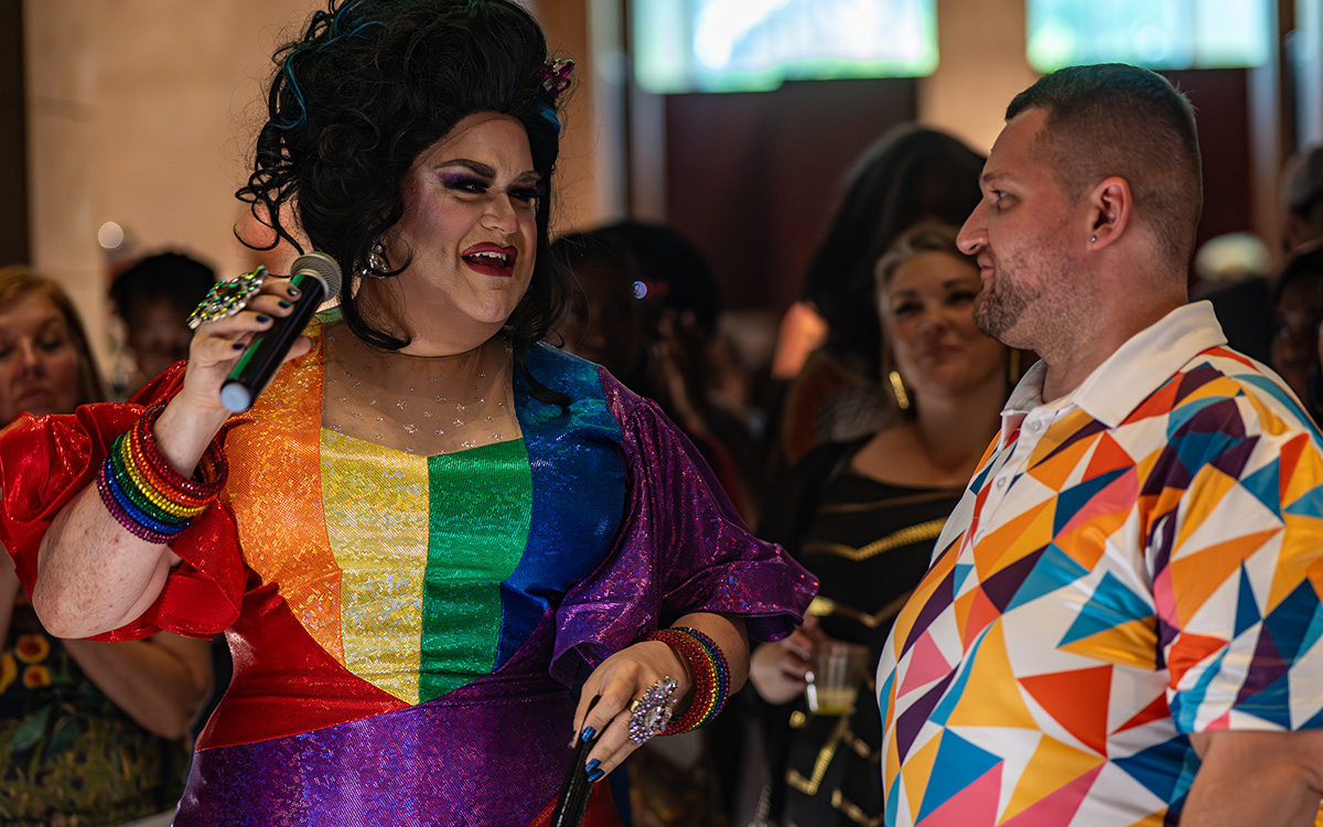 A drag queen in a rainbow dress greets a visitor