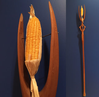 A forked wooden staff adorned with an ear of corn at the tip