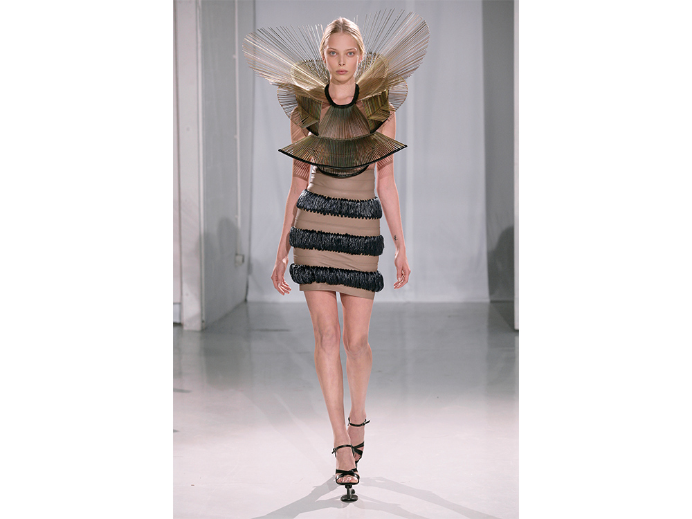 Iris van Herpen's Chemical Crows, Skirt, Collar, a short beige dress with horizontal stripes of a black, fuzzy material. A large circular collar made of long, thin rods extrude out from the neck and around the models head