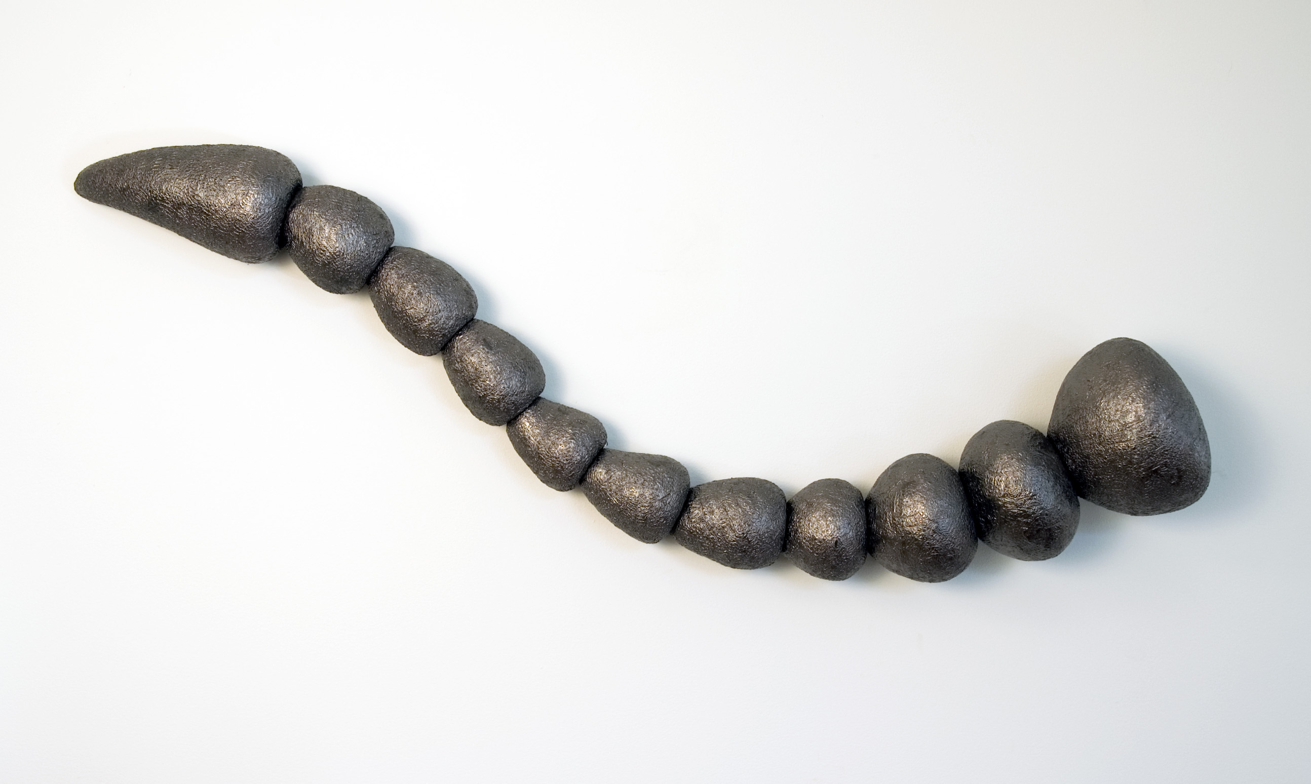 Ana England's Sense, large beads of ceramic connected together forming a tail like structure that comes to a rounded point on the left end