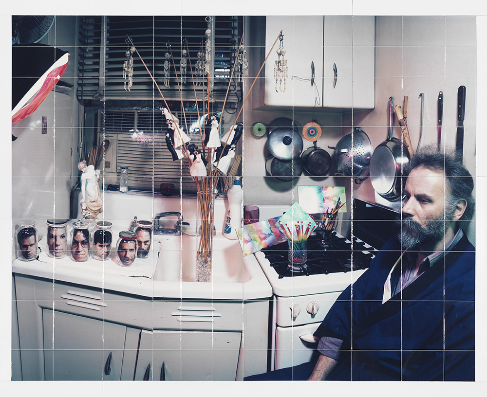 Lucas Samaras' Adjustment, January 22, 1986, a grid of smaller photographs come together like square puzzle pieces revealing the larger image of a man sitting next to his stove facing left. Pots, pans, and utensils hang on the wall behind him. To the left of the stove is a sink and counter top cluttered with jars and bottles with images of faces.