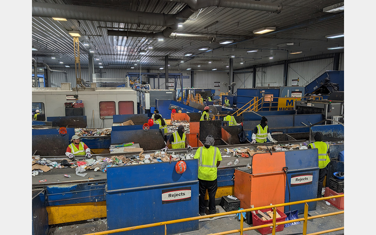 People inside a large warehouse-like space sorting trash on conveyor belts