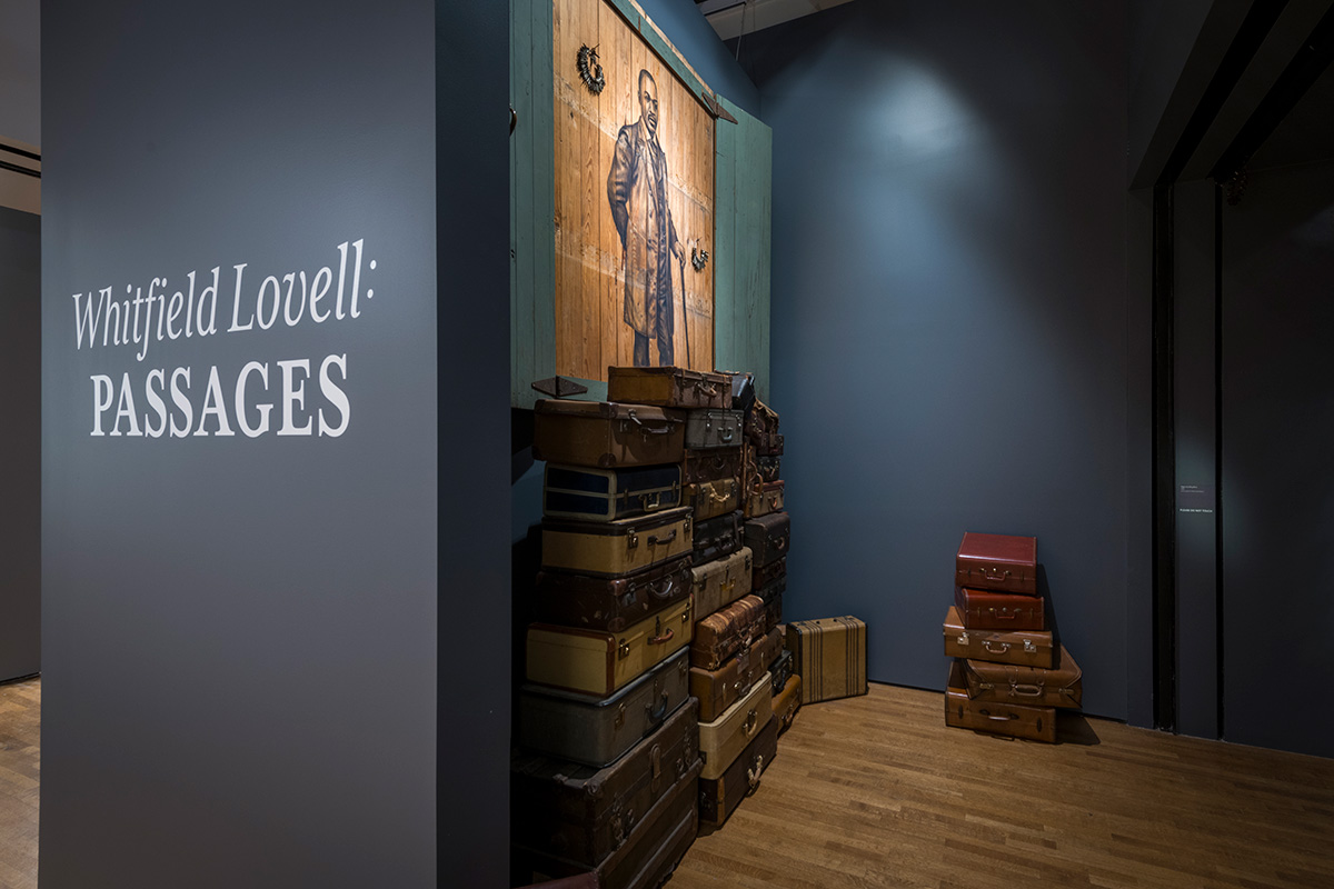 The Whitfield Lovell: Passages title wall, featuring a stack of luggage