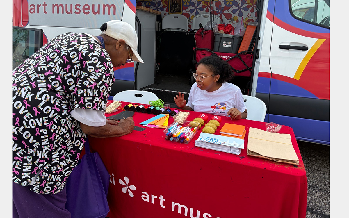 Woman leans over a table while another woman watches what she's doing.