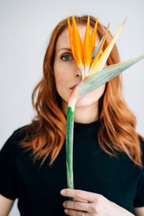 A white woman with red hair posing with an orange flower