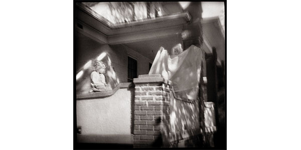 Nancy Rexroth's Playing Ghost, blurry, black and white photograph of two children on a brick banister railing outside of a home. The child on the right is wearing a sheet resembling a ghostly figure