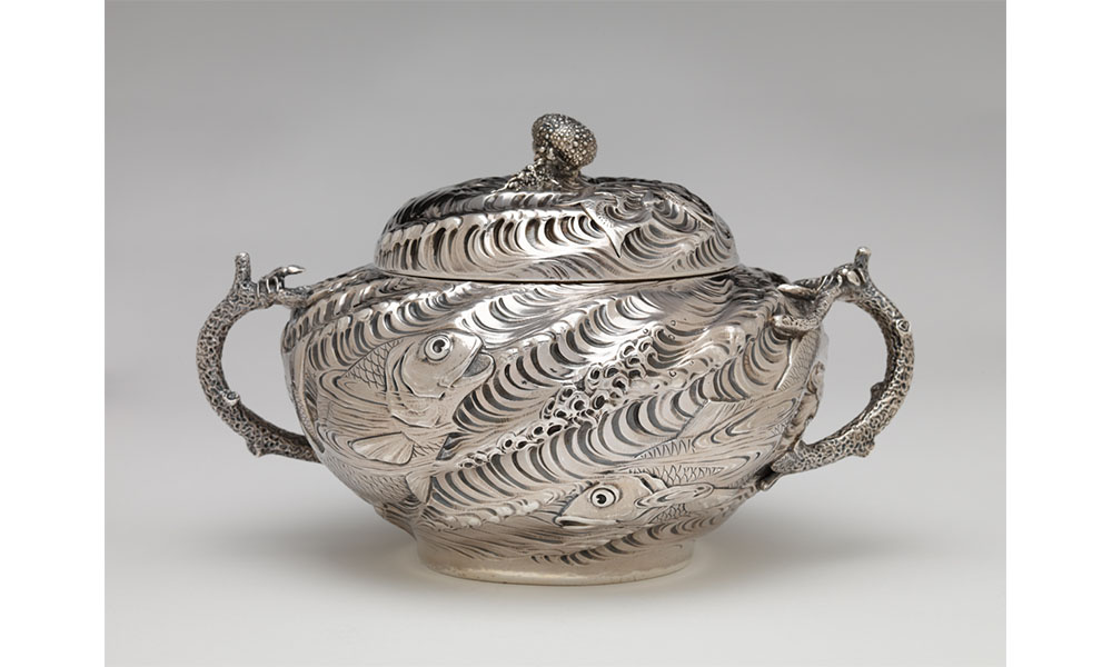 Silver, wavy textured tureen bowl with handles and a lid, decorated with fish