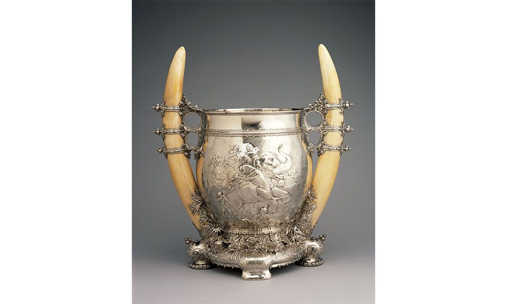 Loving up, a silver chalice with the ends of two elephant tusks on either side for handles. The scene of a tiger attacking an elephant caravan is pressed onto the facade.
