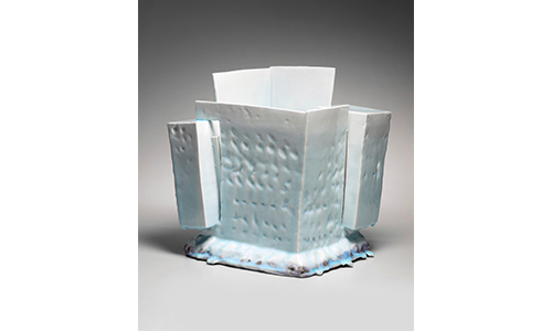 a light blue gradient porcelain cube textured with small divots. Two rectangles jut out from the left and right corners, with the far corner rising higher than the rest. The base flares out giving it a cloud like appearance