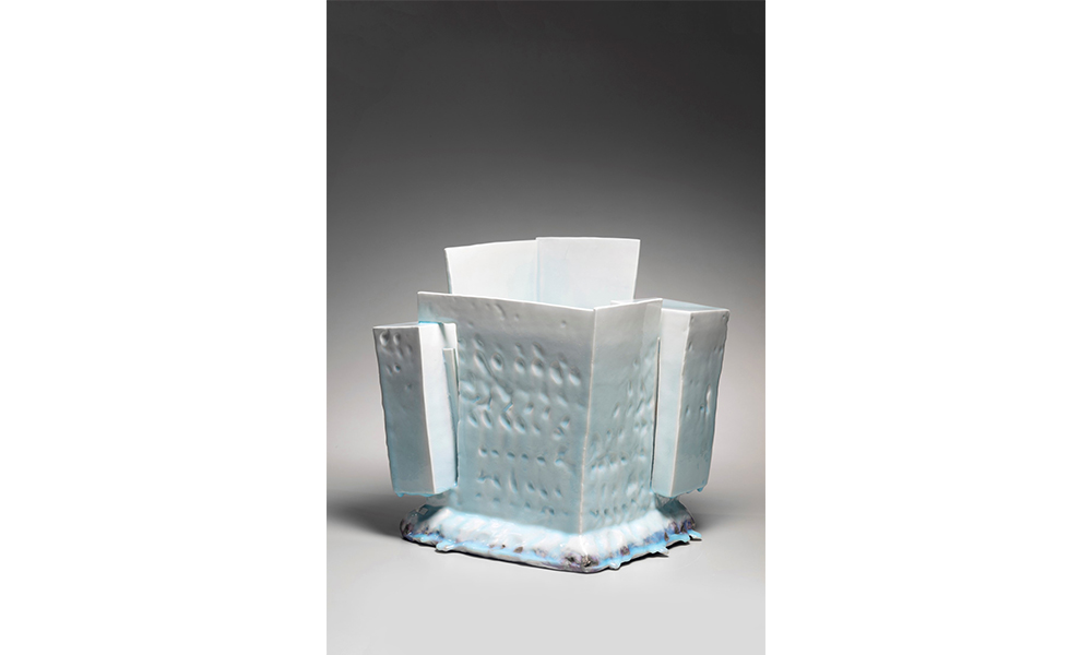 Yoshikawa Masamichi's Kayō (Gorgeous Effigy), a light blue gradient porcelain cube textured with small divots. Two rectangles jut out from the left and right corners, with the far corner rising higher than the rest. The base flares out giving it a cloud like appearance