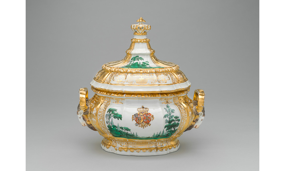 Tureen with Lid, a porcelain pot with gold trim, rams heads for handles, and a green forest scene with a royal coat of arms painted on the side. The lid has a tall crown handle with matching gold trim and green trees