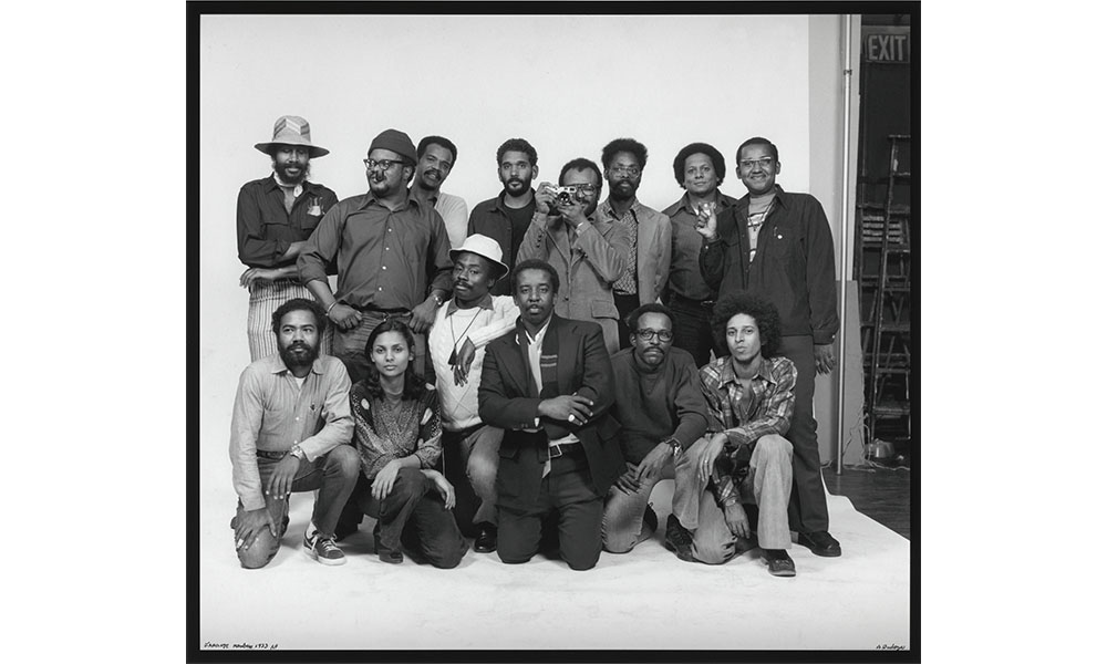 Anthony Barboza's Kamoinge Photographers Group, the all African American photographers groups poses together, a man in the middle holds a camera to his face to take the picture