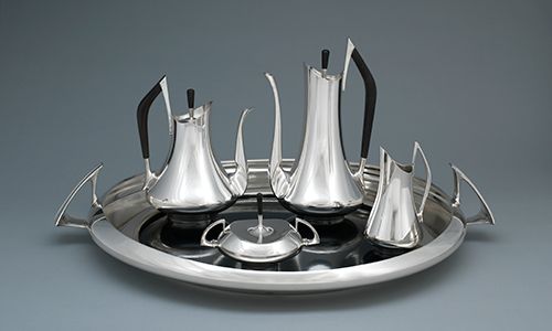 A silver tray with three tall silver pitchers