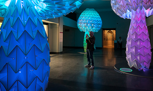 A visitor takes pictures of a massive, colorfully-lit sculpture in the Museum.