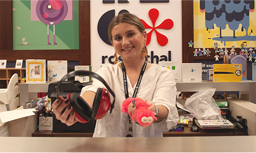 A smiling museum employee holds a pair of headphones and a fidget toy out for the camera.
