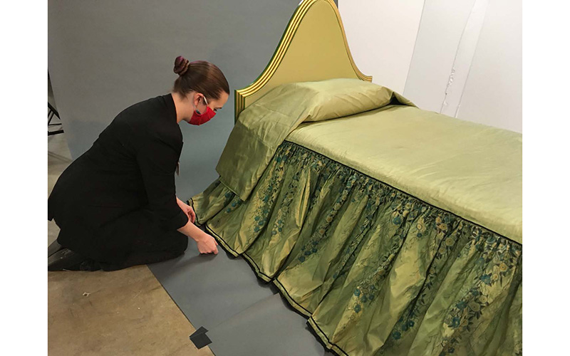 Woman adjusts the skirt of Elaine Wormser's bedspread as it drapes over the bed. 