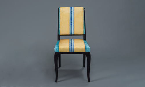 Armless chair with striped upholstery in a blue and yellow variegated striped pattern. 