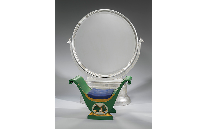 Large standing round mirror on a rectangular silver base. Green seat with gold trim and a blue cushion.