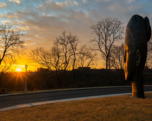 A large black sculpture of a woman's head at sunset