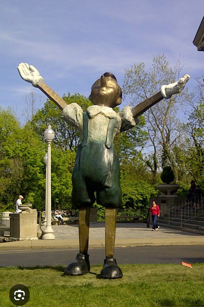 A tall metal sculpture of Pinocchio lifting his arms toward the sky