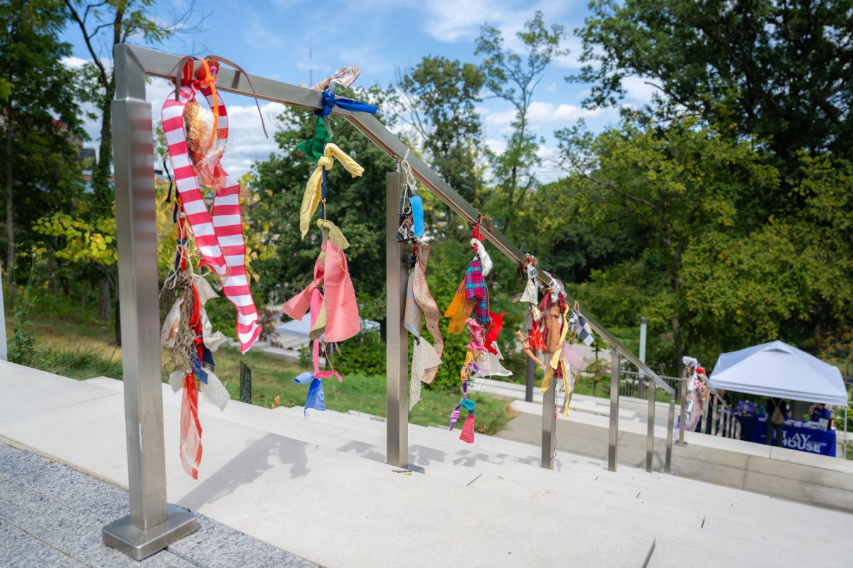 Fabrics wrapped around hand railing descending stone steps on a green hillside.