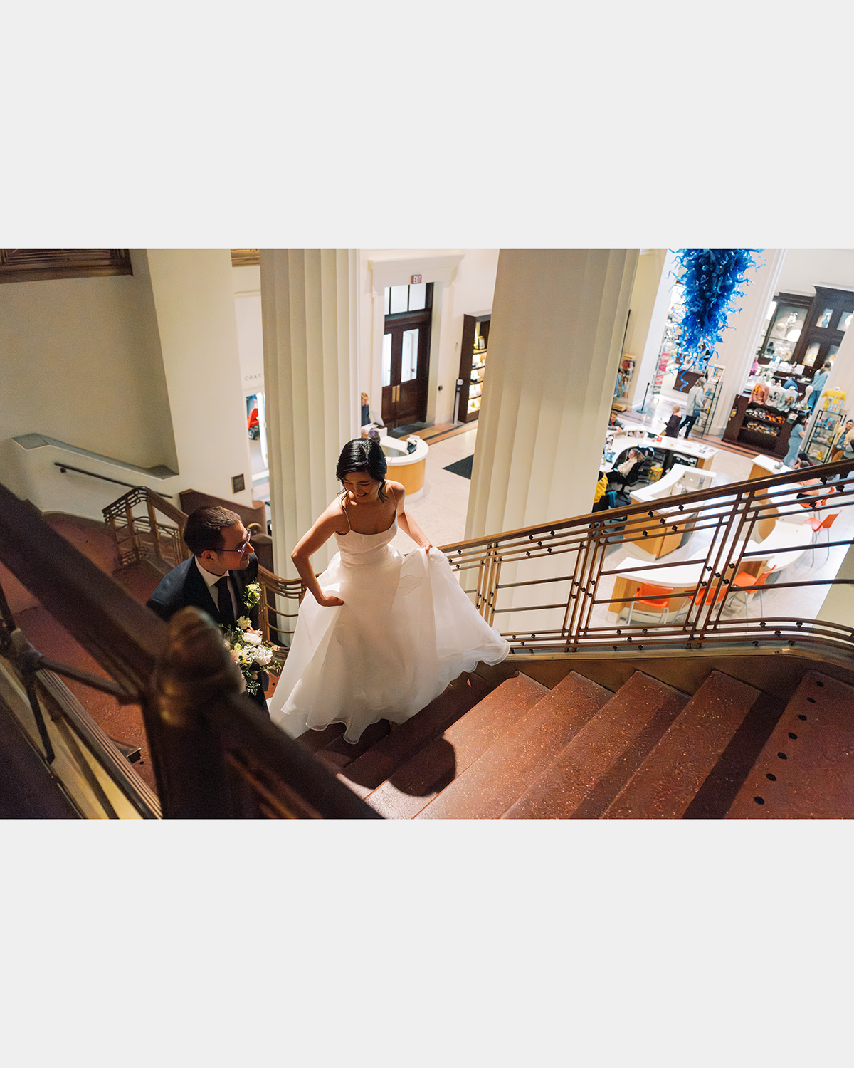 The bride and groom smile as they climb the stairs in the museum