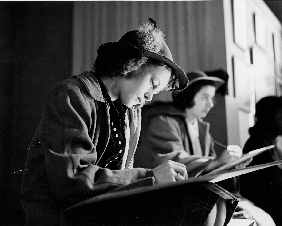 Two well-dress girls from the 1940s draw on drawing boards.