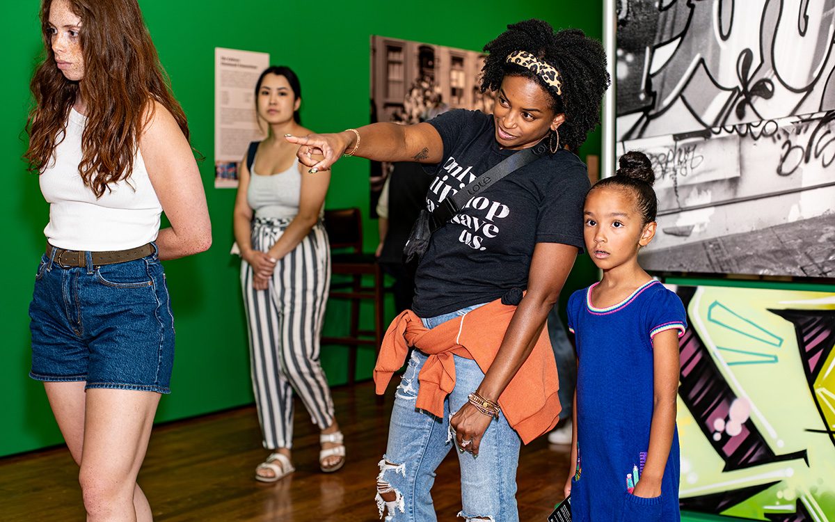A Black mother points to an artwork for her young Black daughter