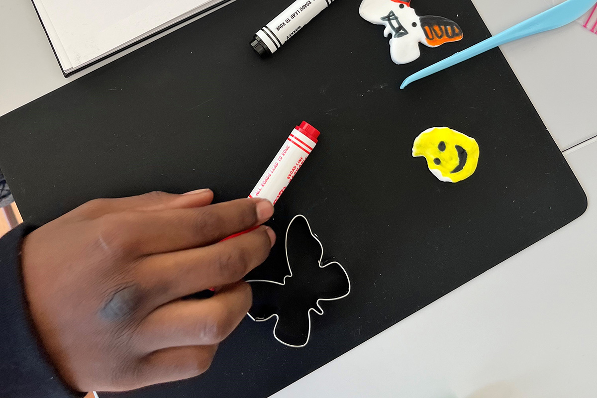 A Black young person's hand holds a marker near some clay art