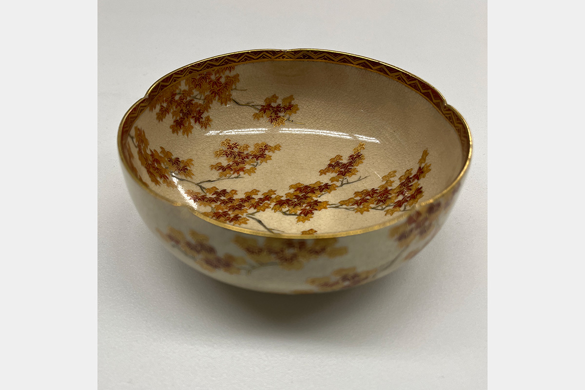 Ceramic bowl featuring a painted design of dark tree branches and brightly colored leaves in hues of red and gold.