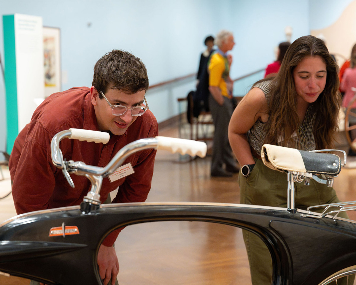 Two white people lean over a swooping black bicycle