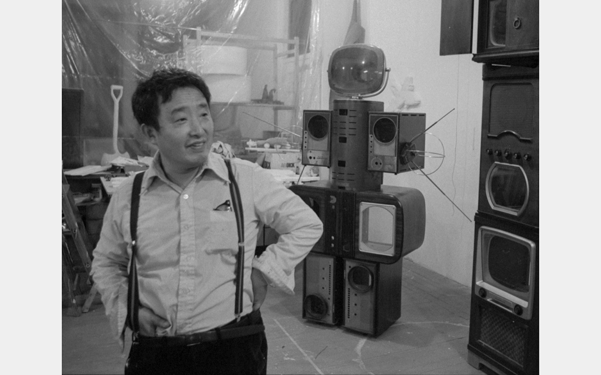 Man with suspenders stands near piled TV sets