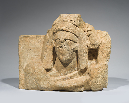 A stone carving including a damaged face with long hair