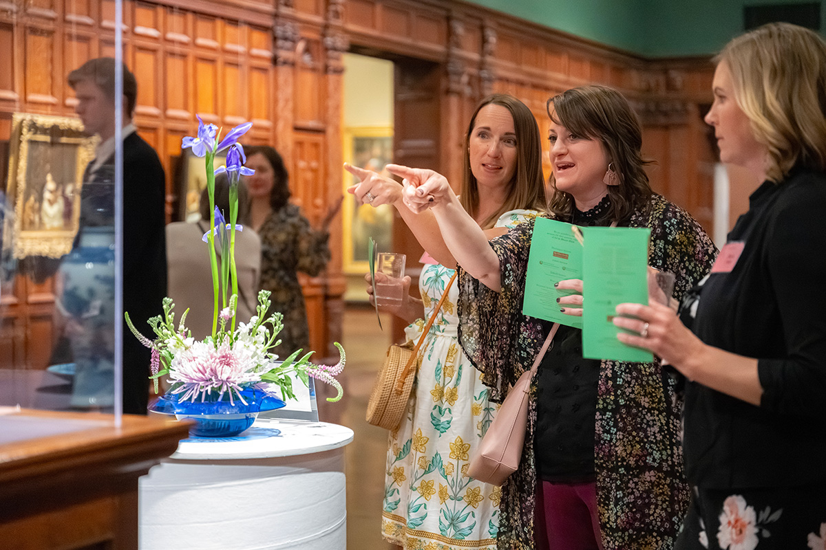 A group of white women smile and point at a floral arrangement