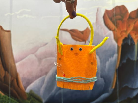 A human hand holds an animal-like figure made of yard against the backdrop of a landscape painting.